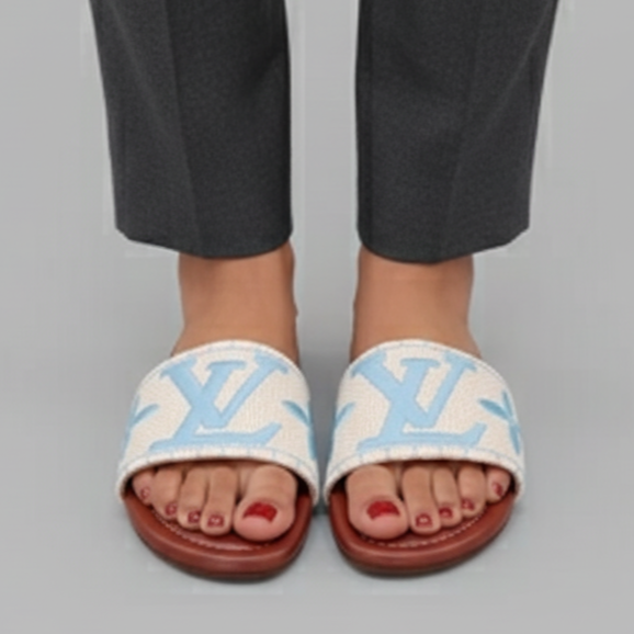 White slides with blue logo worn by a person in black pants on a gray background