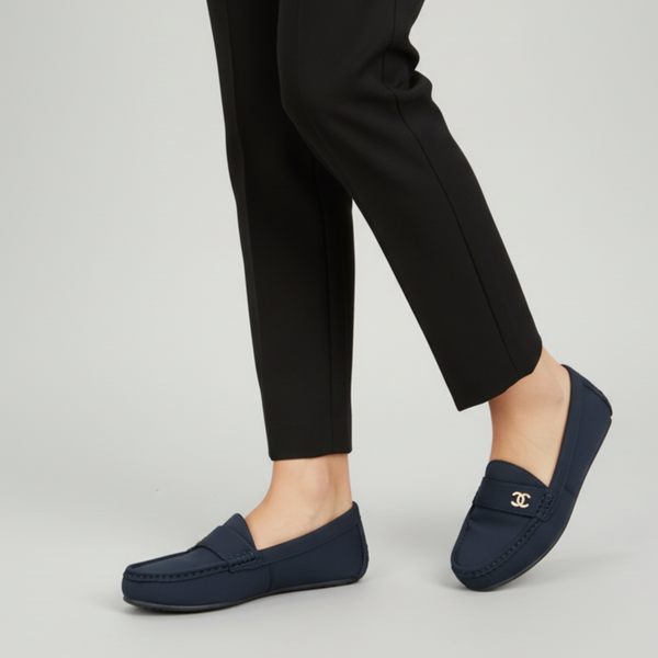 Navy loafers with a brand logo worn with black pants on a light gray background