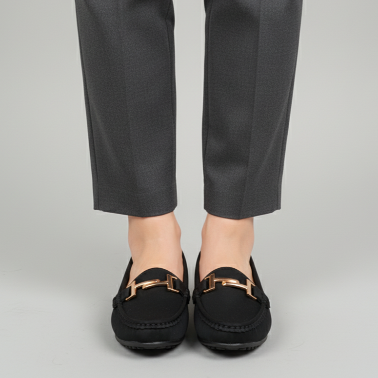Person wearing black loafers with gold accents and gray pants on a light gray background