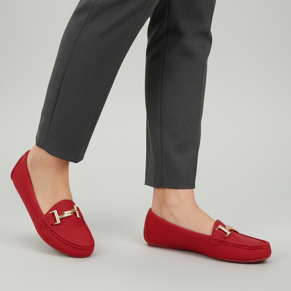 Red loafers with gold accents worn with gray pants on a light gray background