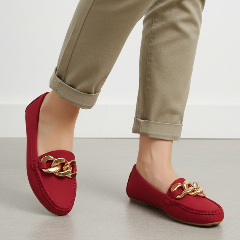 Red loafers with gold chain detail worn by a person in beige pants on a light background