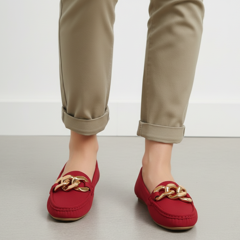 Red loafers with gold chains worn by a person on a light gray floor.