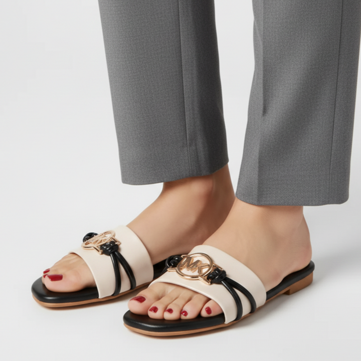 White sandals with black straps and gold accents worn with gray pants on a white background