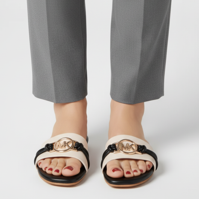 White sandals with black soles and gold logo worn with gray pants on a white background