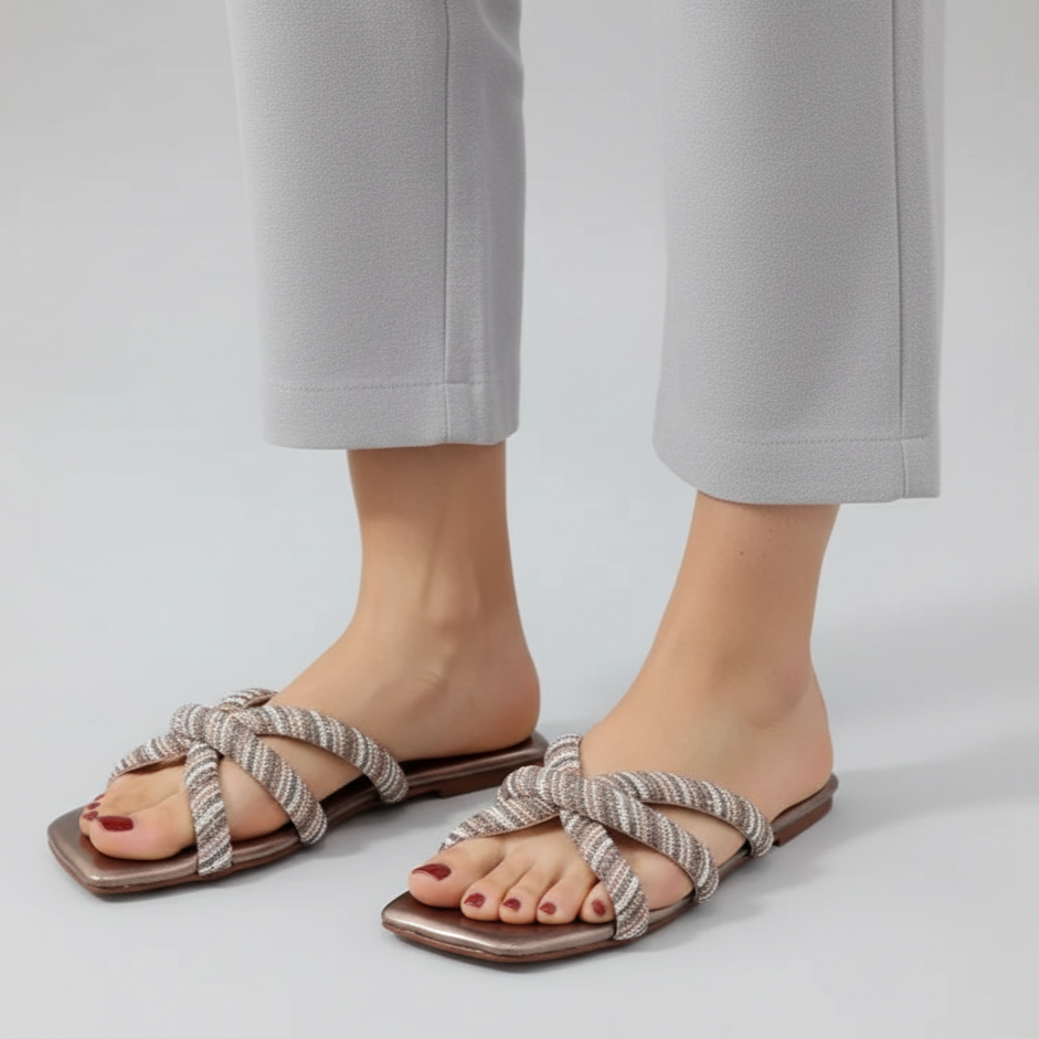 Pair of sandals worn with light gray pants on a plain background