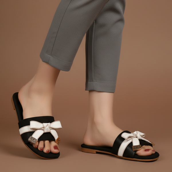 Black sandals with white bows worn by a person on a brown background