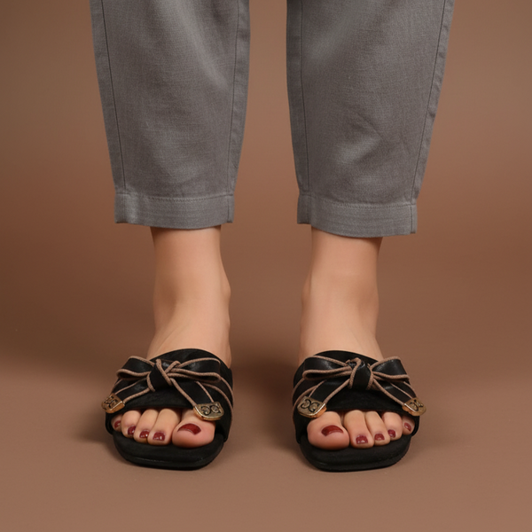 Person wearing gray pants and black sandals with gold accents on a brown background