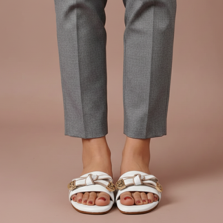 Person wearing gray pants and white sandals with gold accents on a beige background