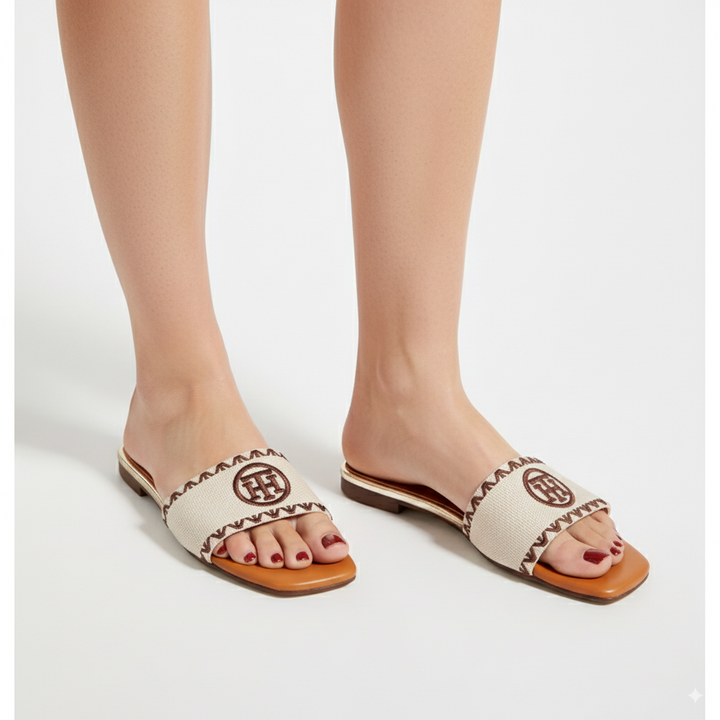 White sandals with brown soles and decorative straps worn by a person on a white background