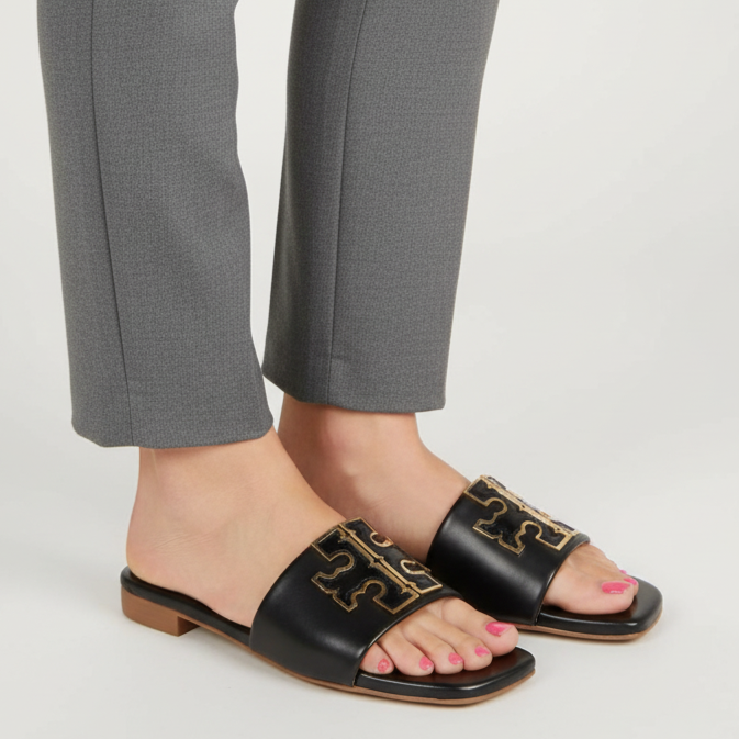 Person wearing black sandals with gold detailing and gray pants on a white background