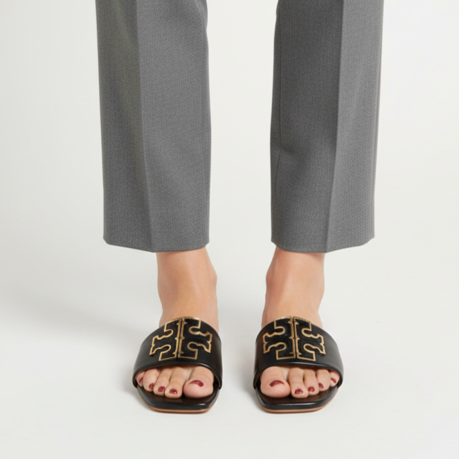 Person wearing gray pants and black sandals with gold accents on a white background