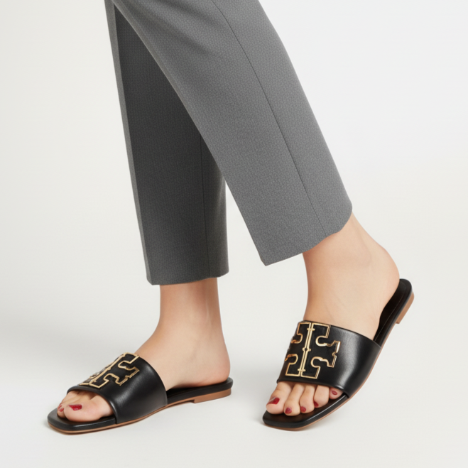 Person wearing black sandals with gold detailing and gray pants on a white background