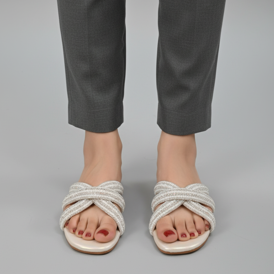 White sandals with braided design worn with gray pants on a gray background