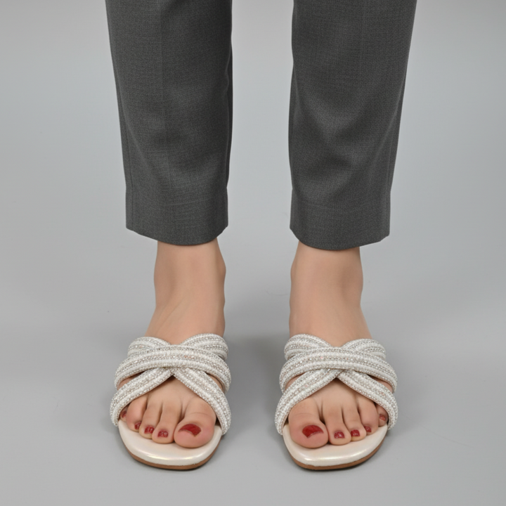 White sandals with braided design worn with gray pants on a gray background