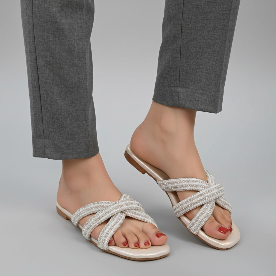 White sandals with criss-cross straps worn with gray pants on a neutral background