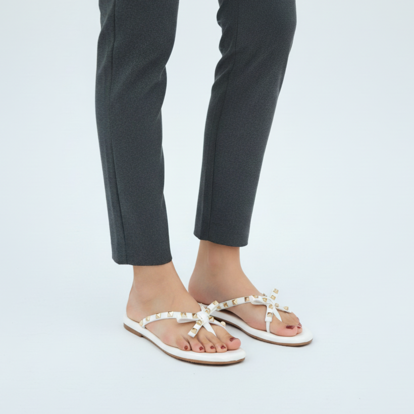 Person wearing white sandals with bow details on a plain background