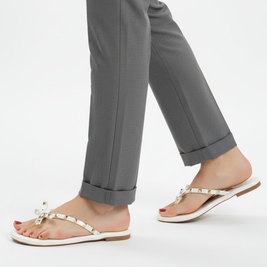 Person wearing gray pants and white sandals with decorative straps on a white background