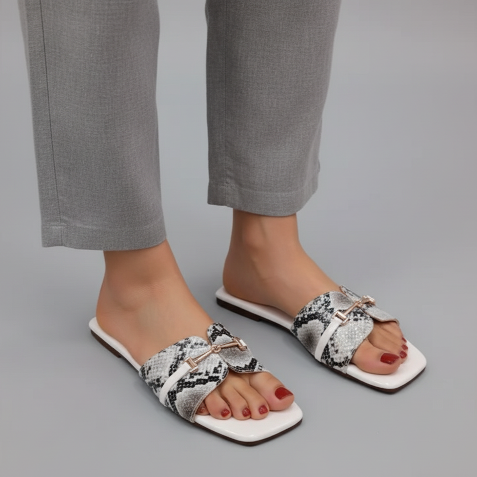 White sandals with black and white pattern worn with gray pants on a gray background