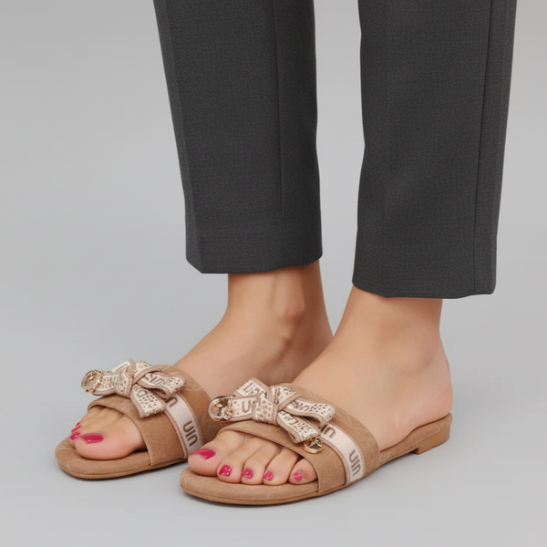 Brown sandals with decorative bows worn with black pants on a gray background