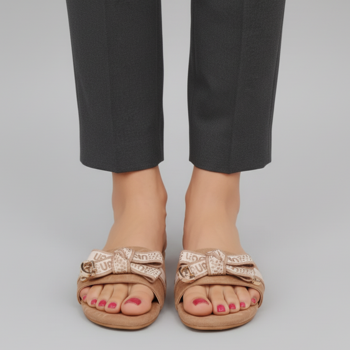 Beige sandals with decorative straps worn with black pants on a gray background