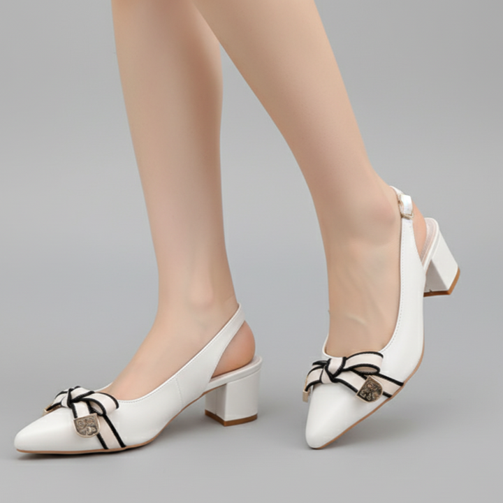 White high-heeled shoes with black bow design worn by a person on a gray background