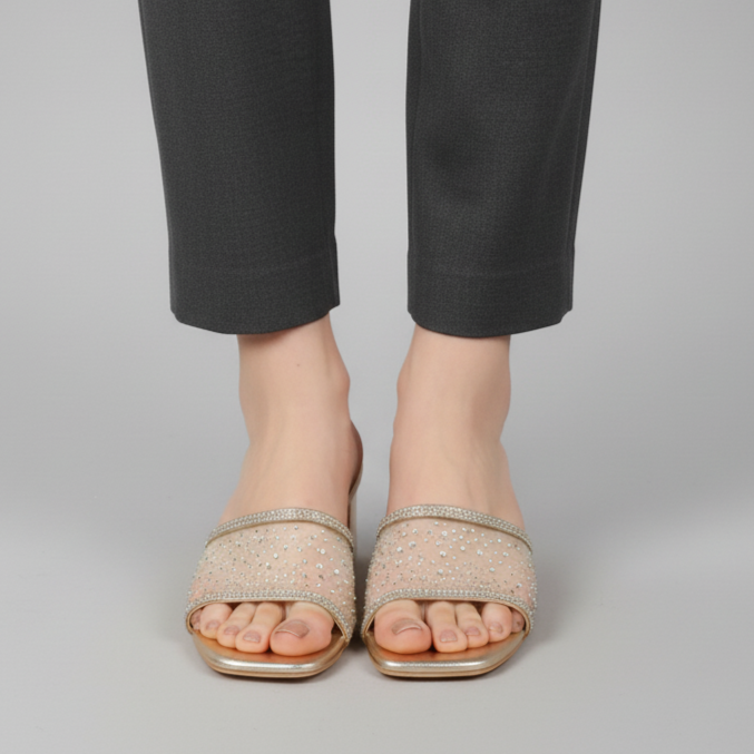 Person wearing black pants and beige open-toe sandals on a gray background