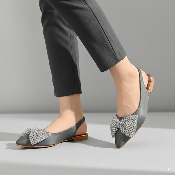 Gray flat shoes with decorative bows worn with black pants on a neutral background