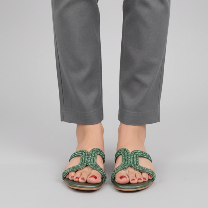 Person wearing gray pants and green sandals on a plain background