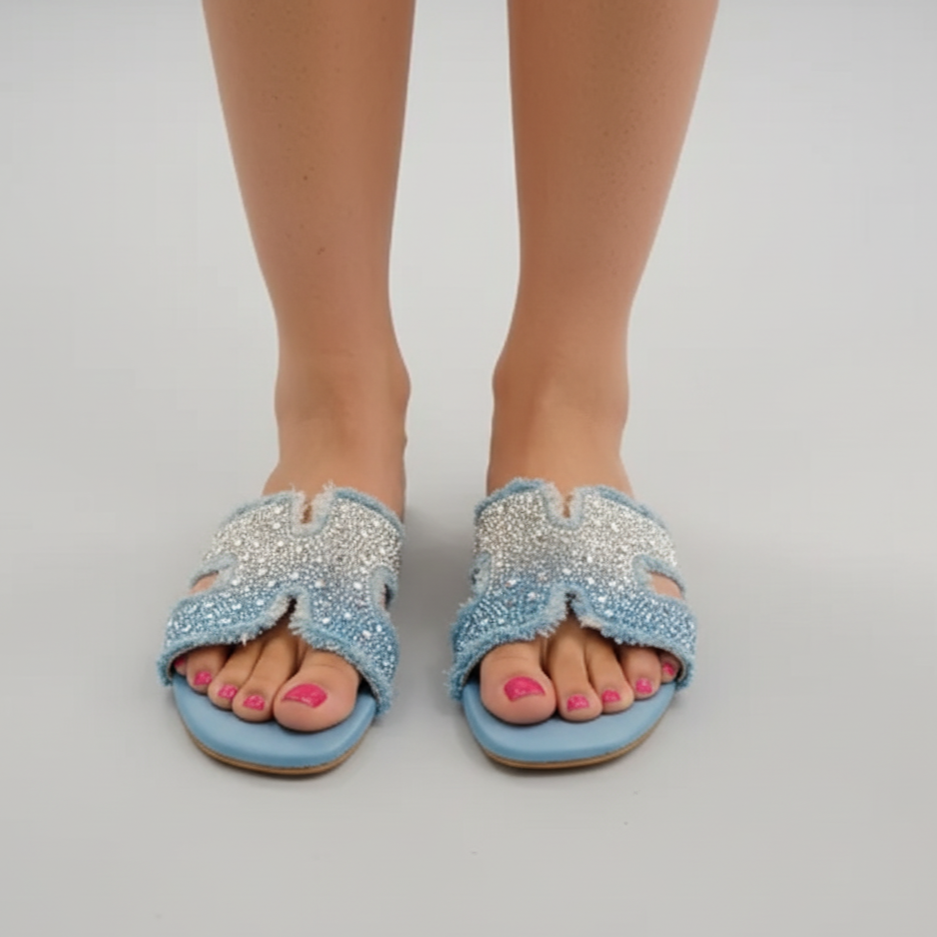 Blue sandals with rhinestone embellishments worn by a person on a light gray background