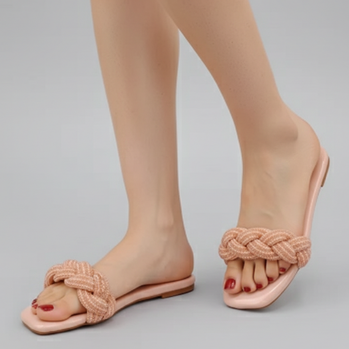Pink sandals with braided design worn by a person on a gray background