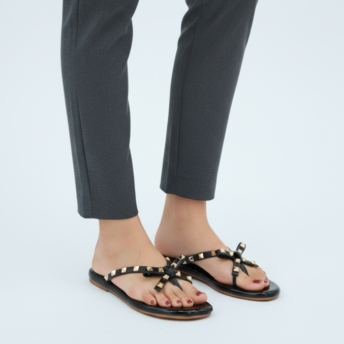 Black studded sandals worn with gray pants on a white background