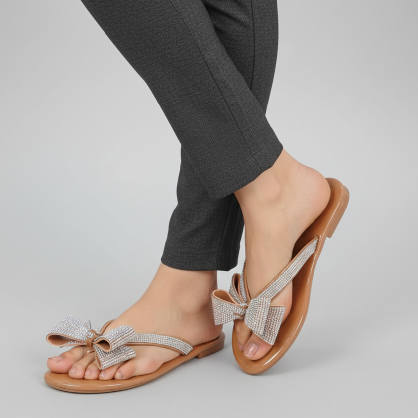 Brown sandals with decorative bows worn with dark gray pants on a light gray background