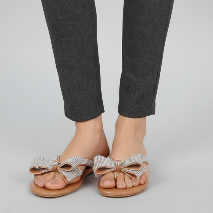 Person wearing gray pants and sandals with decorative bows on a plain background
