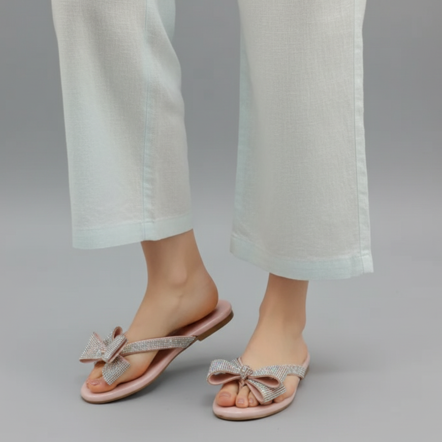 Person wearing light pink sandals with bow details on a gray background