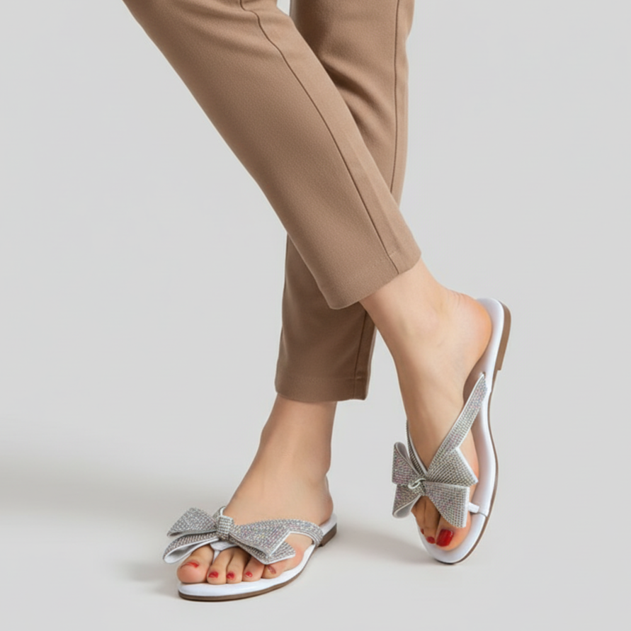 Silver sandals with bow details worn with beige pants on a light gray background