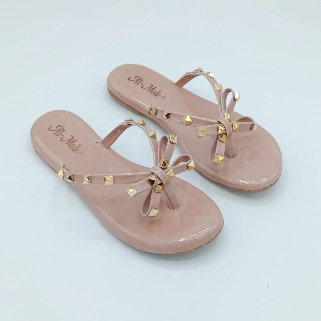 A pair of beige slip-on shoes with gold studs, displayed against a white background.
